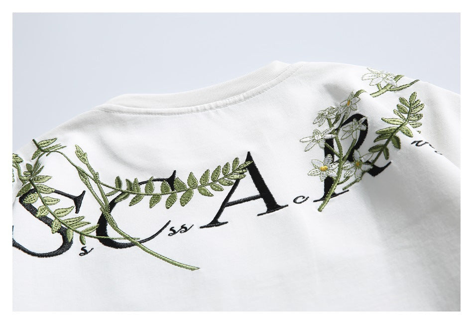 Close-up of the back of a white shirt with black lettering and green floral embroidery.