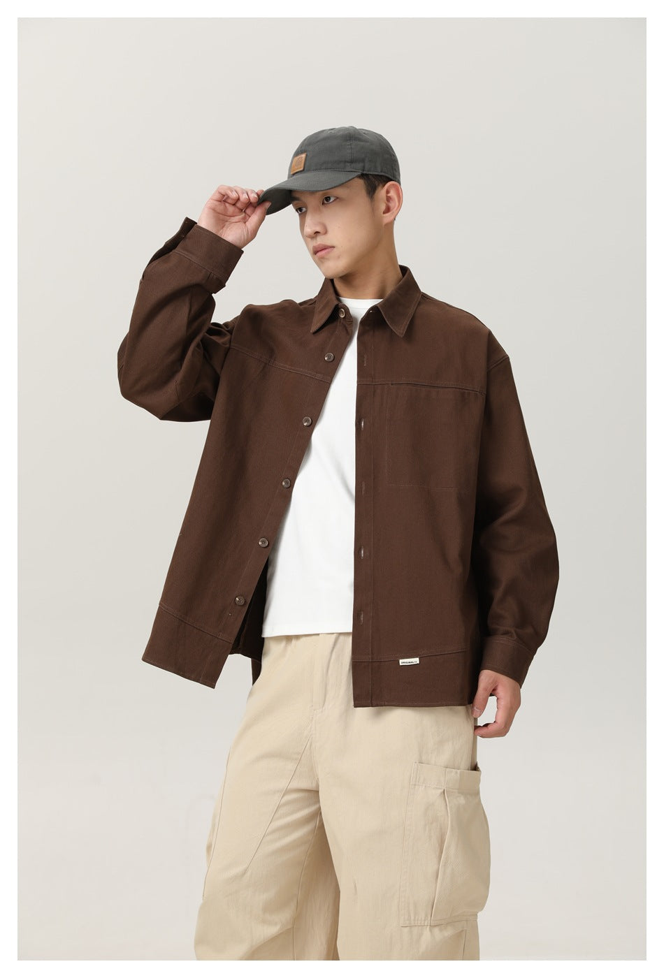 Model wearing an open dark brown button-front shirt jacket over a white tee, with cream cargo pants.