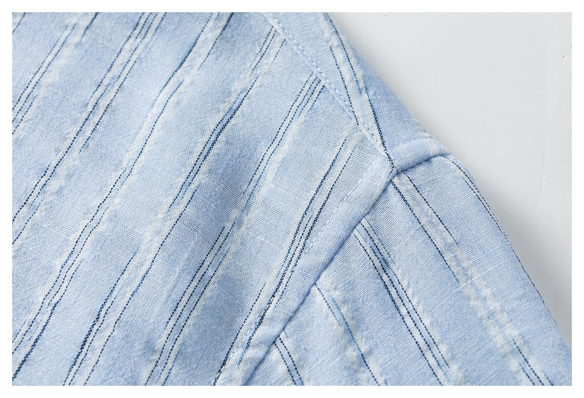 Close-up of pale blue fabric with narrow navy stripes and a diagonal stitched seam.