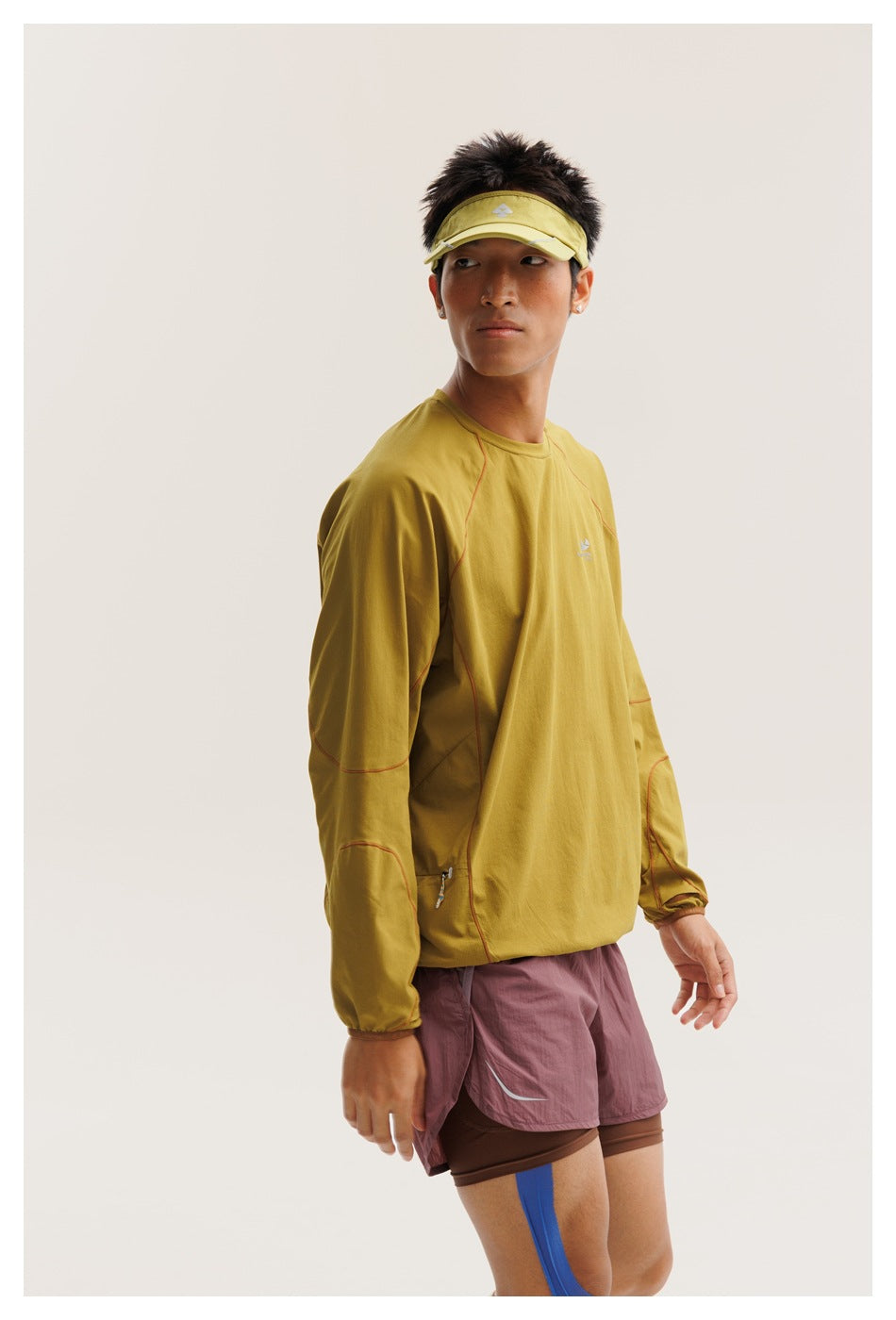 Three-quarter view of a model wearing a mustard-yellow long-sleeve top with red seam accents and mauve shorts.