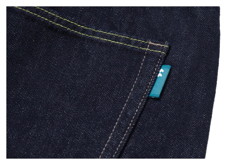 Close-up of a dark indigo denim pocket with yellow-green topstitching and a small turquoise fabric tab.