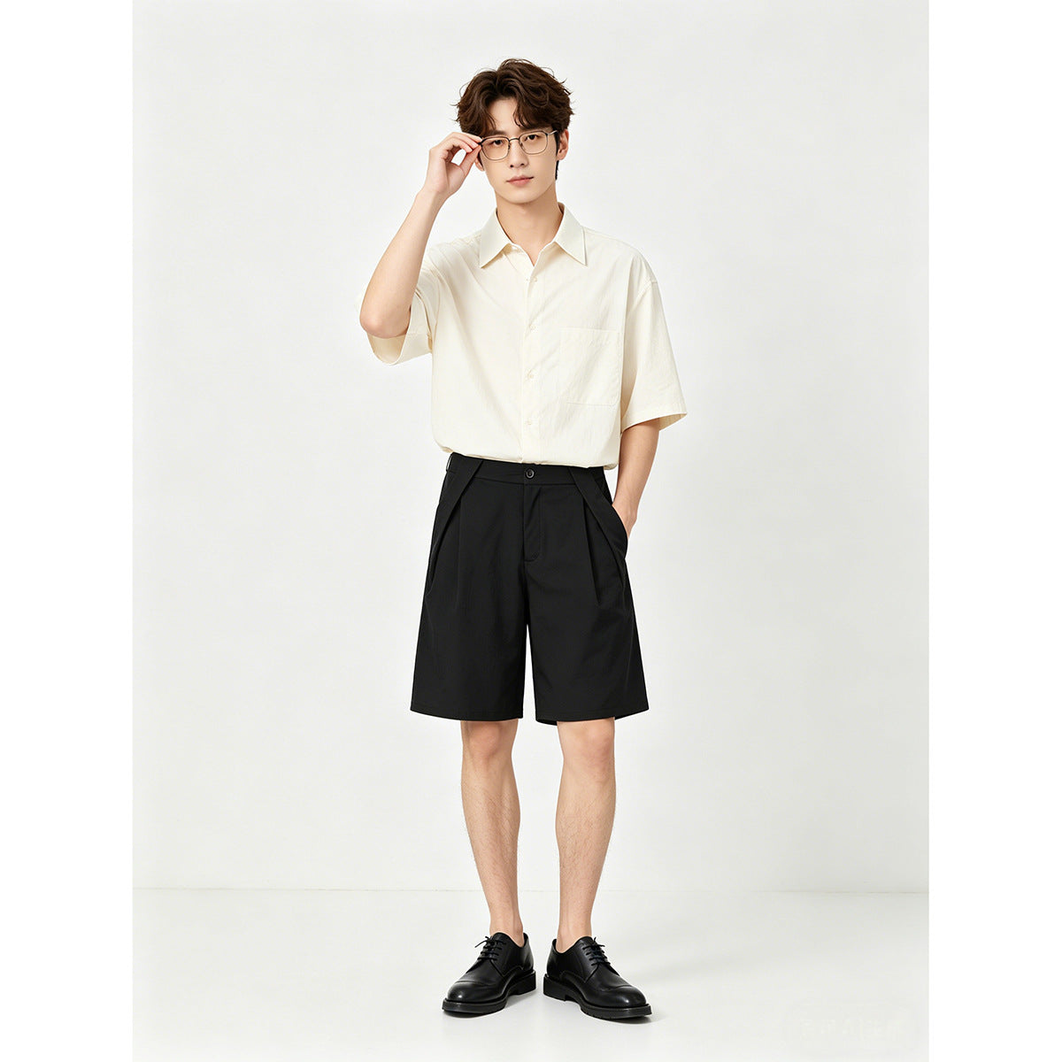 Model wearing an ivory short-sleeve button-up shirt and black pleated shorts, front view.