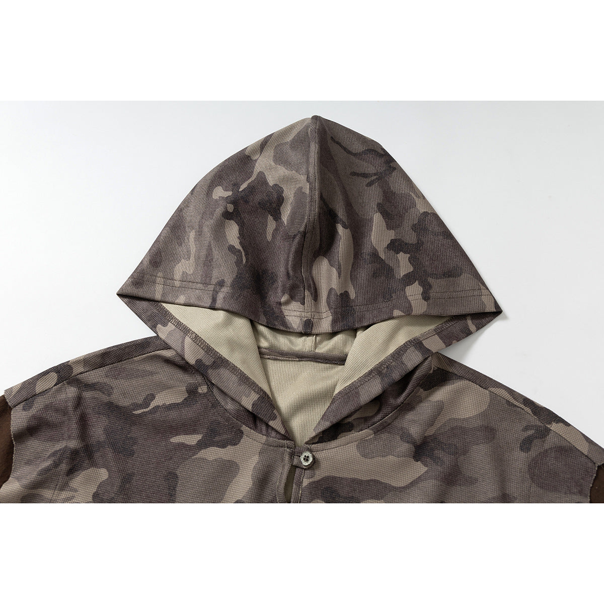 Close-up of a gray-brown camouflage hood and upper chest with a light lining and single-button neckline.