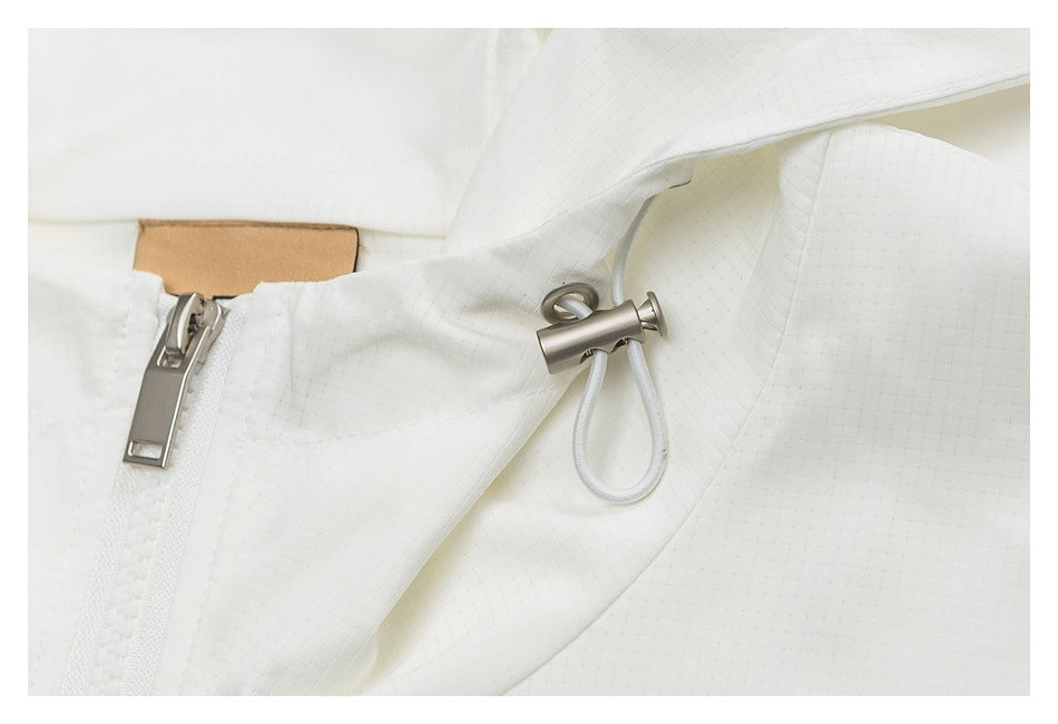 Close-up of the white jacket's zipper and metal drawcord toggle against subtly grid-textured fabric.