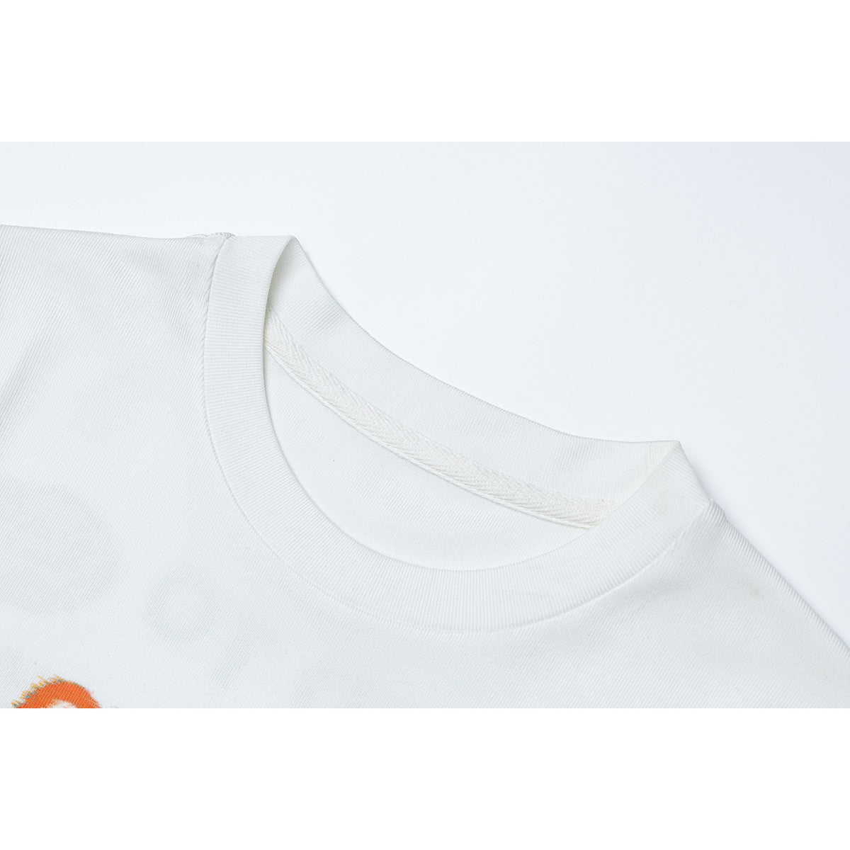 Close-up of a white T-shirt's ribbed crew neckline and shoulder seam, with a small orange print edge visible.