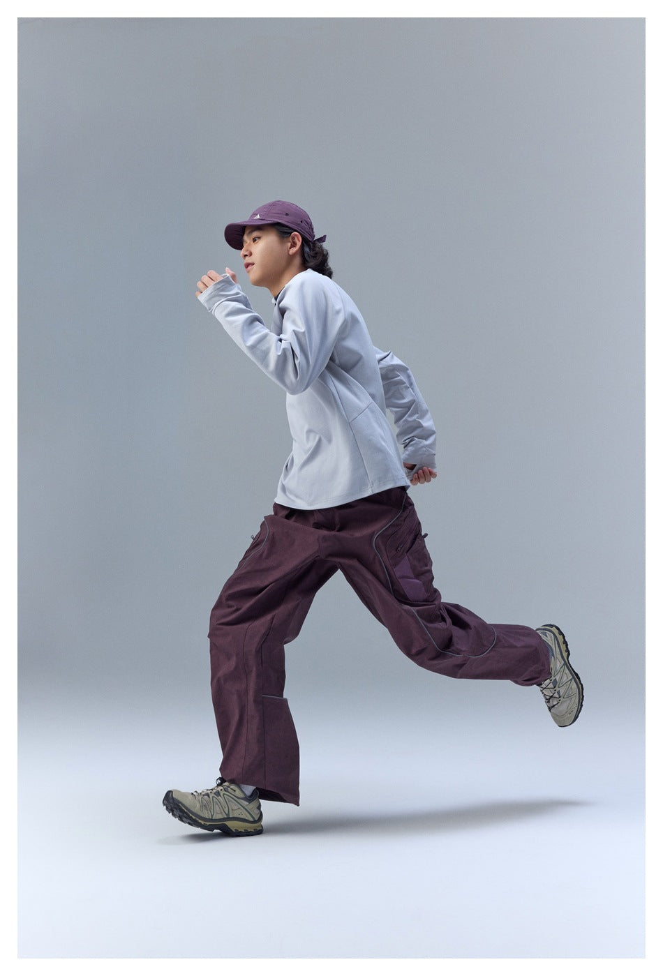 Model running in a light gray long-sleeve top, plum cargo pants, and a matching plum cap.