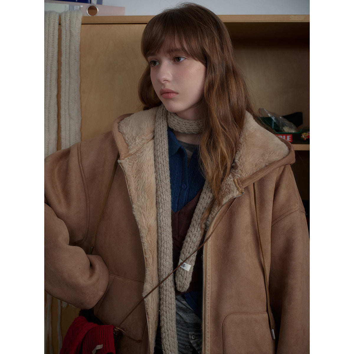 Close view of a model in a tan jacket with cream plush lining, layered over a blue top and chunky beige scarf.