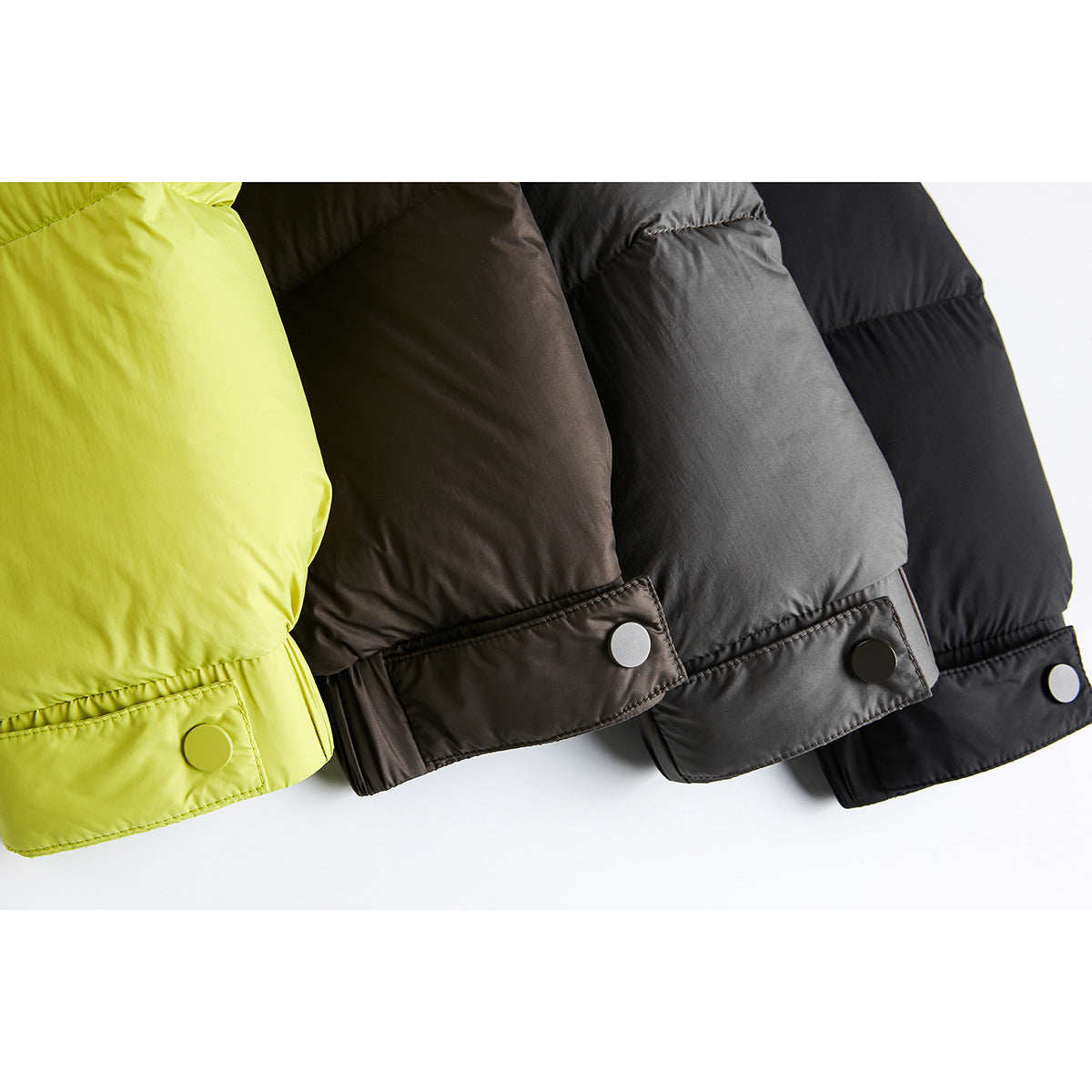 Close-up of the lower hems and snap-button tabs of lime, brown, charcoal, and black padded jackets.