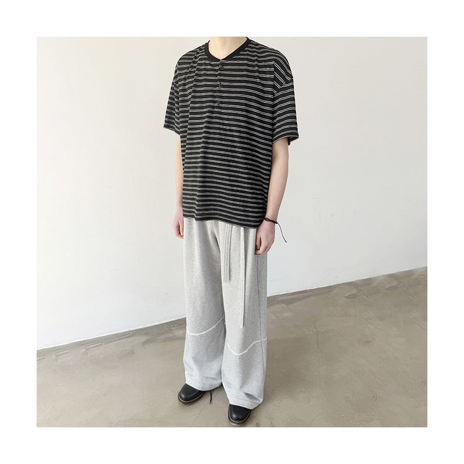 Model wearing black striped short-sleeve Henley T-shirt with light gray wide-leg sweatpants and black shoes, cropped at face