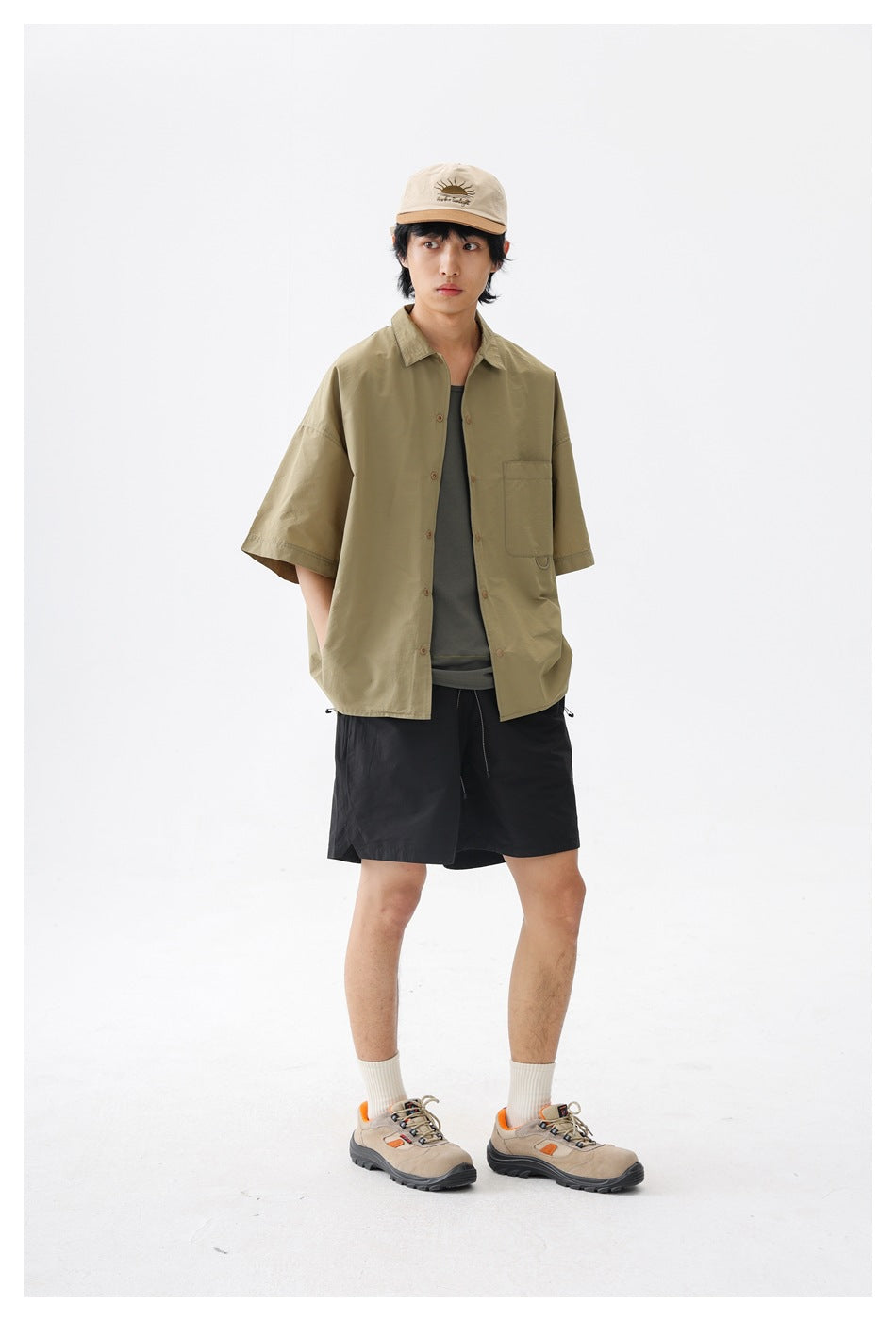 Model wearing an oversized olive short-sleeve button-up shirt with a chest pocket, layered over a dark top.