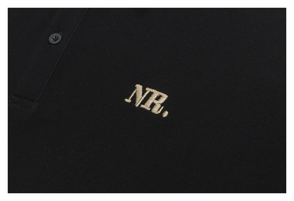 Close-up of beige NR embroidery on the chest of a black polo shirt.