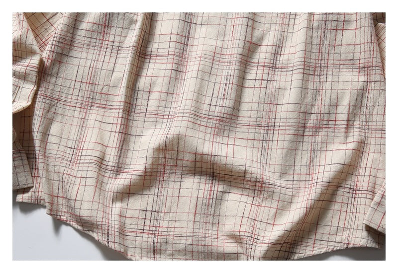 Close view of cream fabric with a fine red and gray plaid pattern and a softly folded hem.