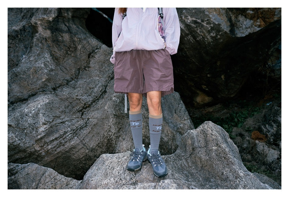 Front view of a hiker wearing mauve shorts, a pale jacket, gray socks and blue-gray hiking shoes.