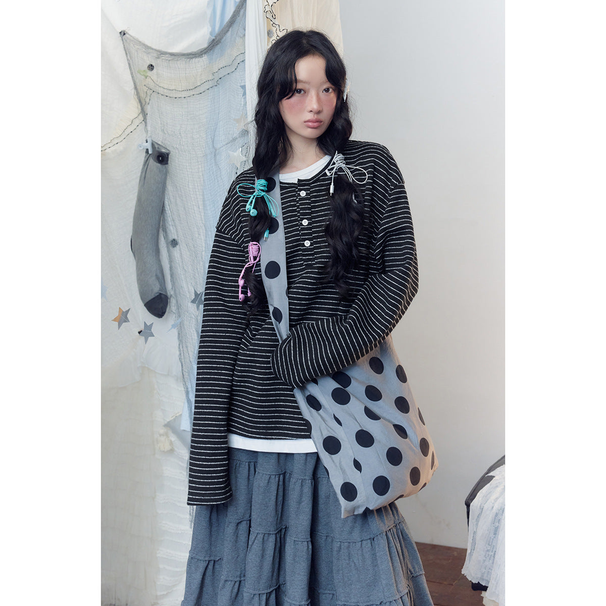 Closer view of a model in a black-and-white striped henley and gray polka-dot shoulder bag.