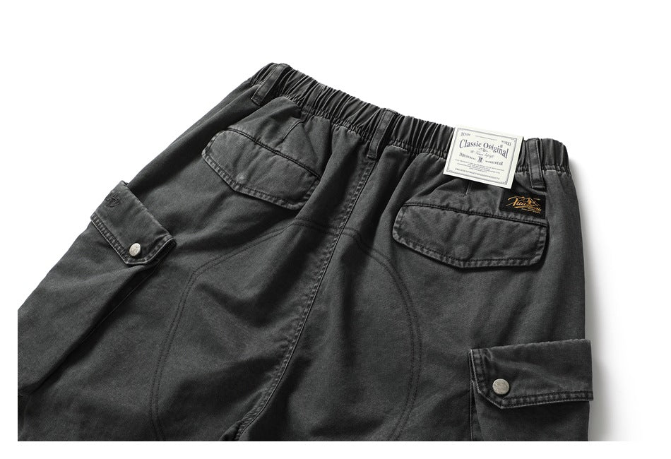 Rear view of charcoal cargo shorts with an elastic waist, flap pockets and attached tags.