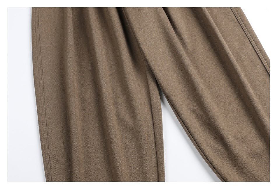 Close-up of taupe trousers showing the drape and seams along the overlapping legs.