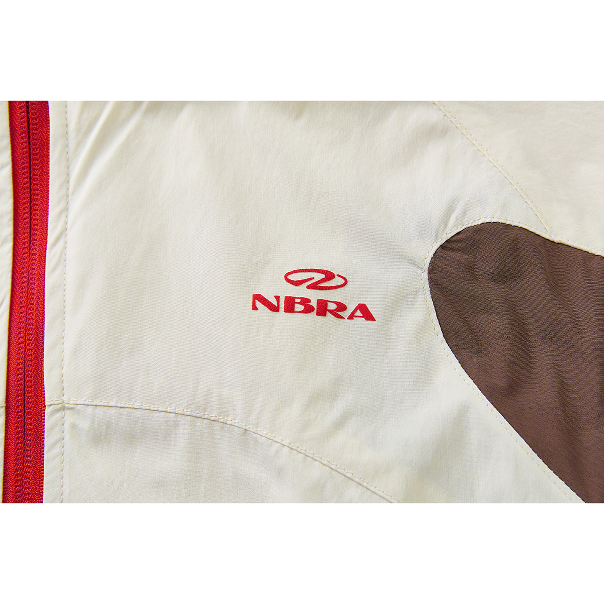 Close-up of a cream jacket with a red zipper, brown panel and red NBRA logo on the garment.