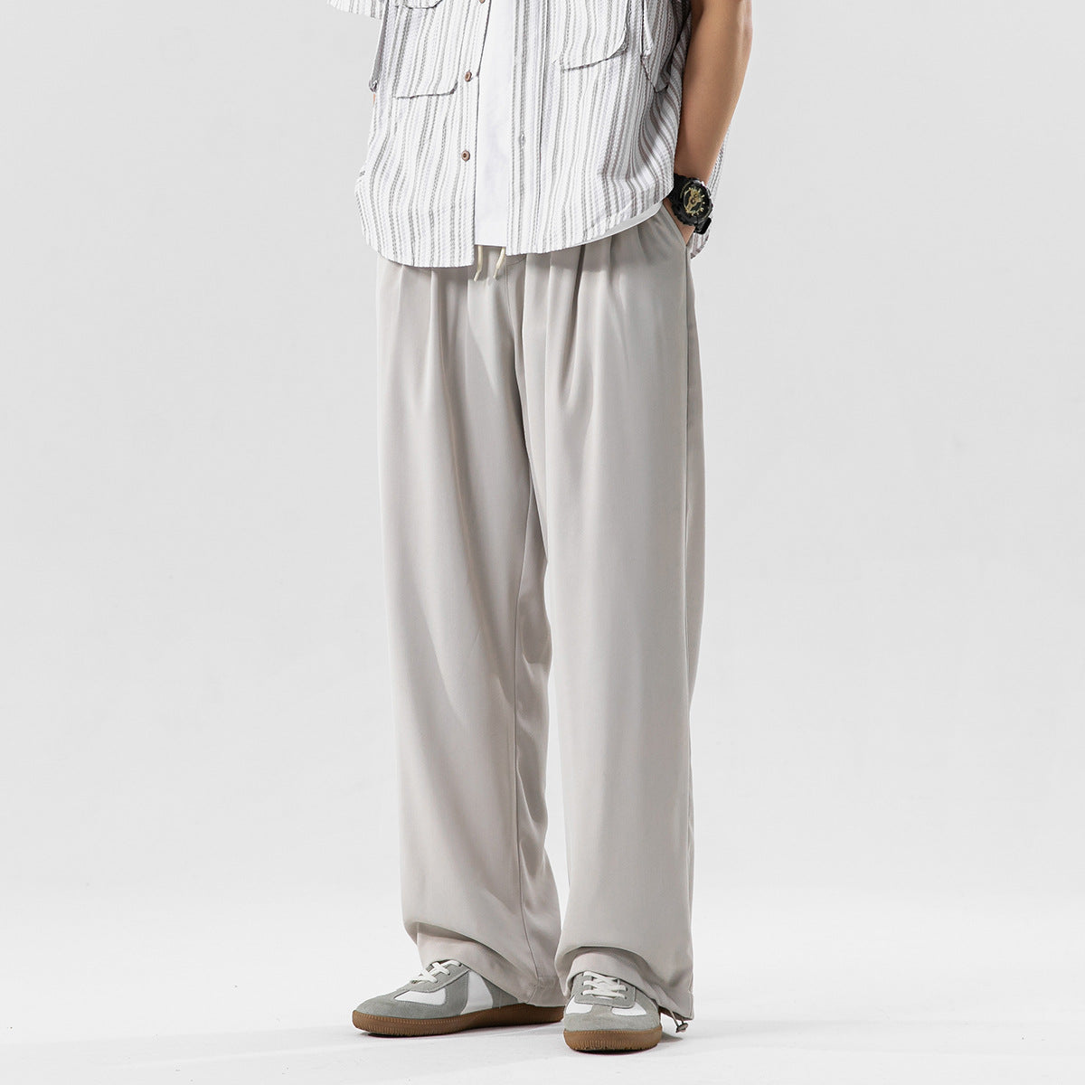A person wears loose pale gray trousers with long, wide legs and sneakers, shown from waist to feet.
