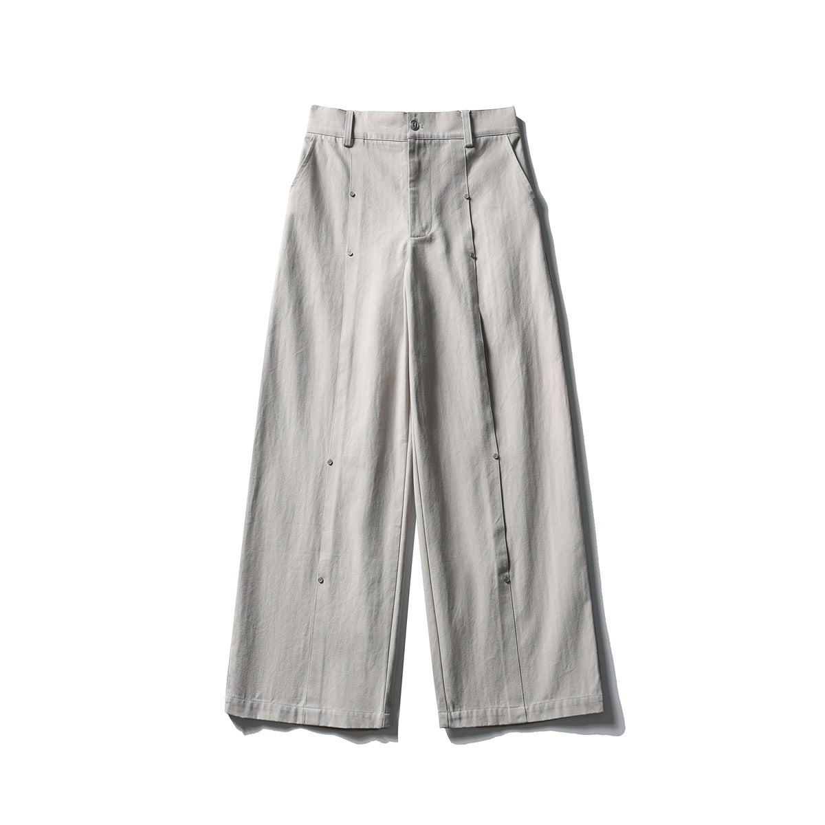 Light gray wide-leg pants flat lay, front view with zip fly, belt loops, side pockets and stud details on the leg seams