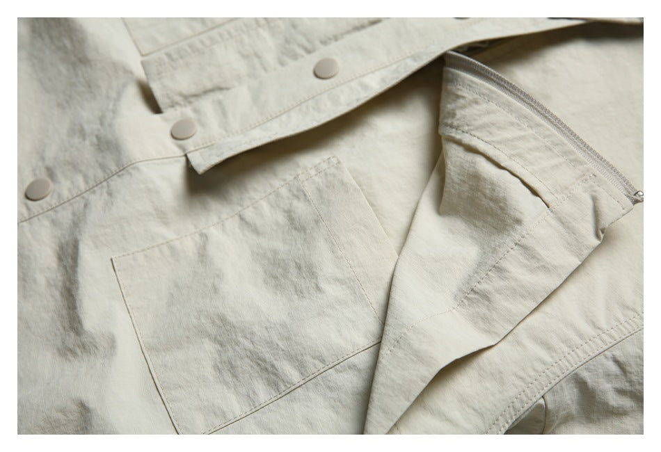 Close-up of the light beige jacket's patch pocket, snap-button front, and partially open zippered chest pocket.