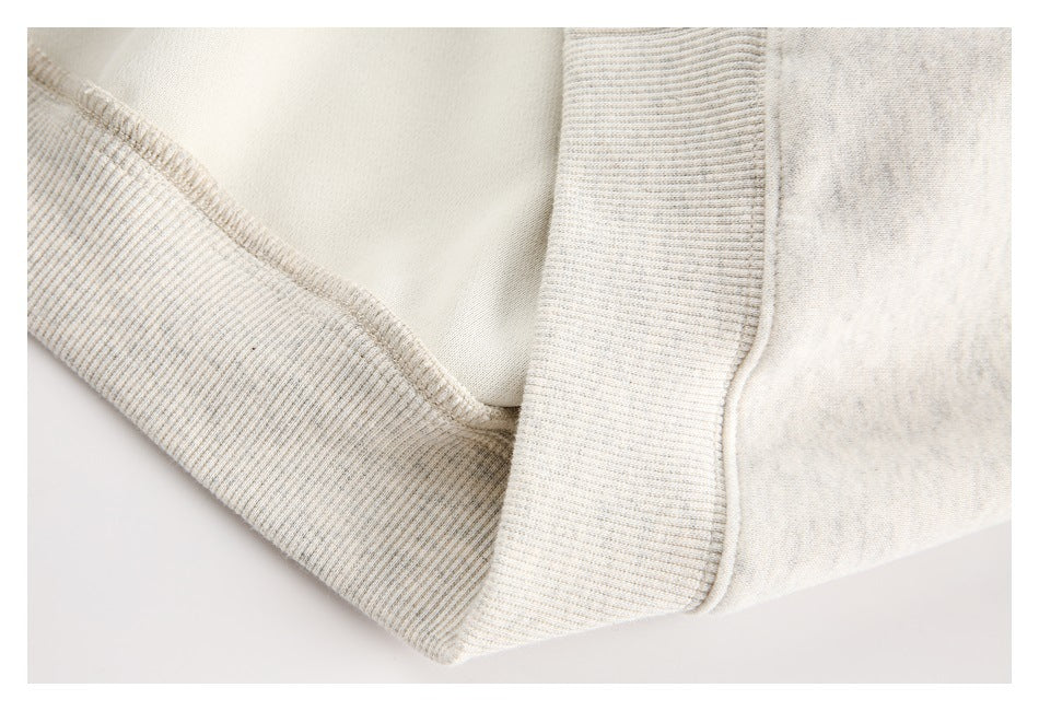 Close-up of an ivory heather sweatshirt showing ribbed trim and a stitched seam.