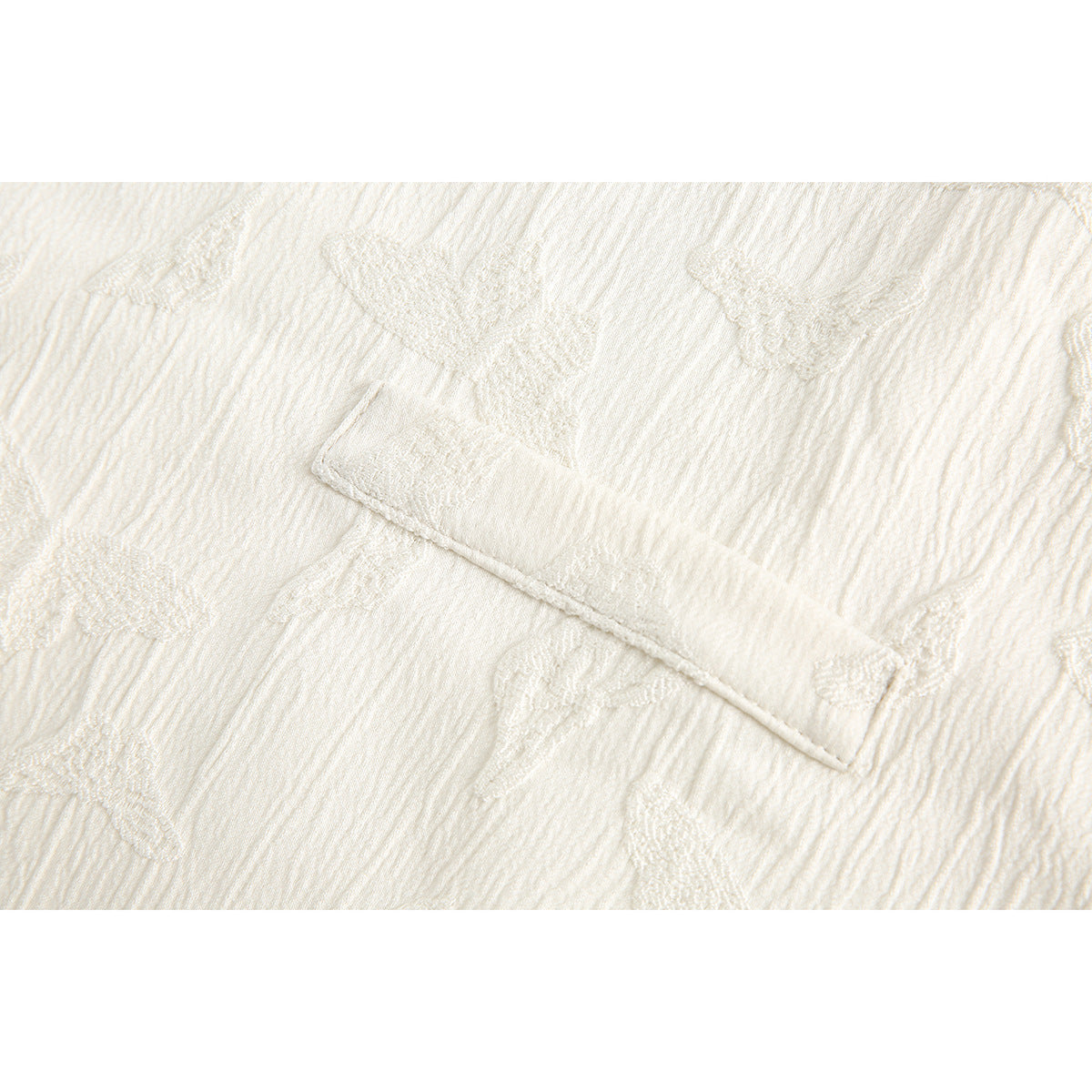 Close-up of a small rectangular pocket on white textured fabric with raised tonal motifs.