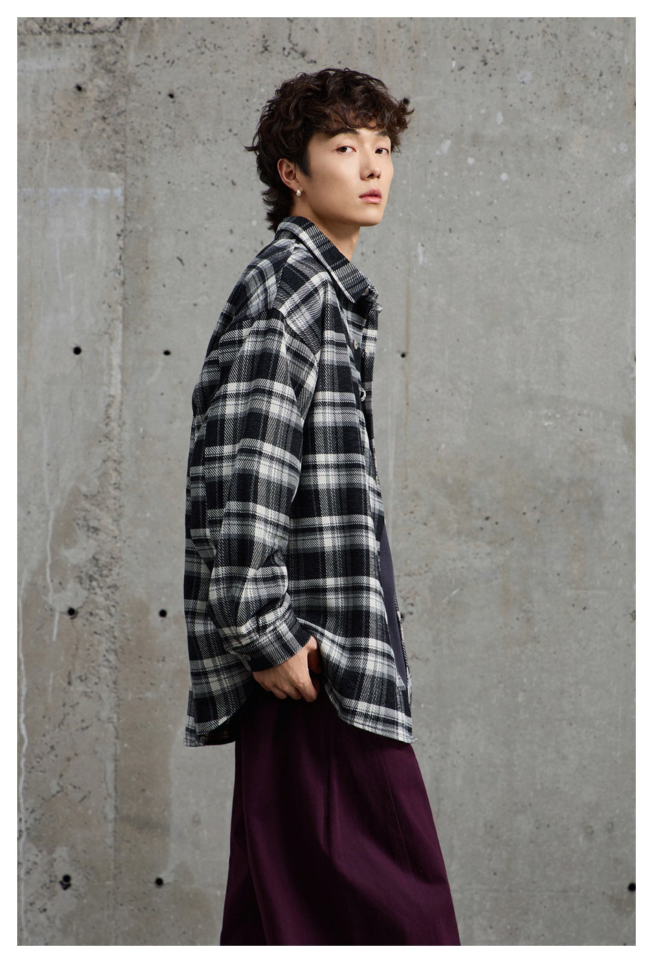 Closer side view of a model wearing a loose black-and-white plaid button-up shirt.