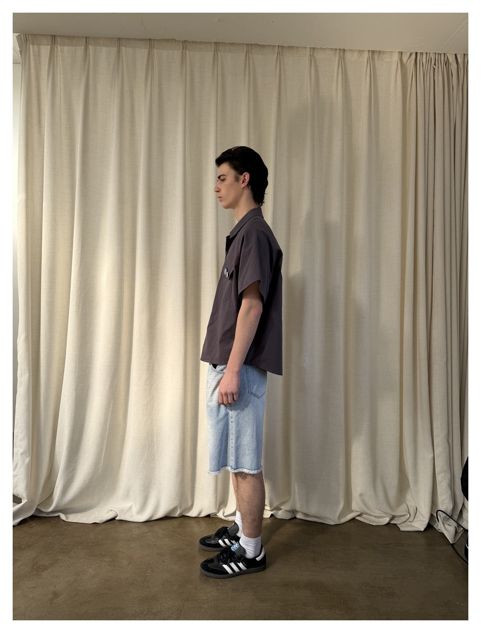 Side view of model wearing dark gray short-sleeve shirt with light wash denim shorts and black sneakers
