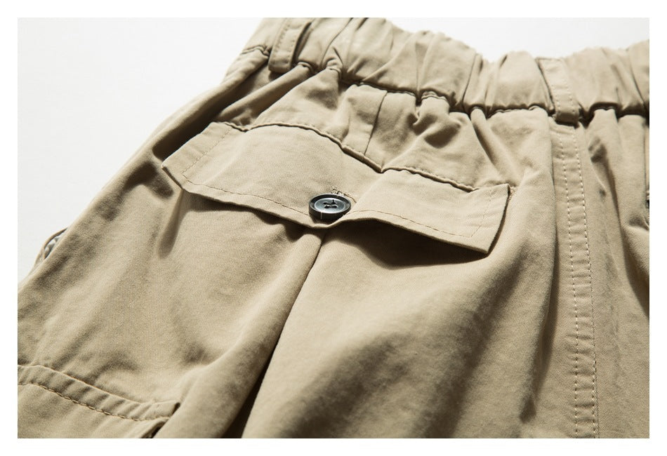 Close-up of khaki trousers showing a gathered elastic waistband and a buttoned flap pocket.