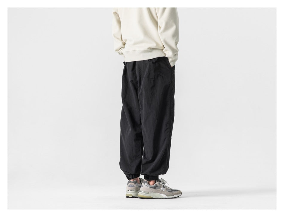 Model wearing black loose-fit jogger pants with elastic cuffs, shown from the back.