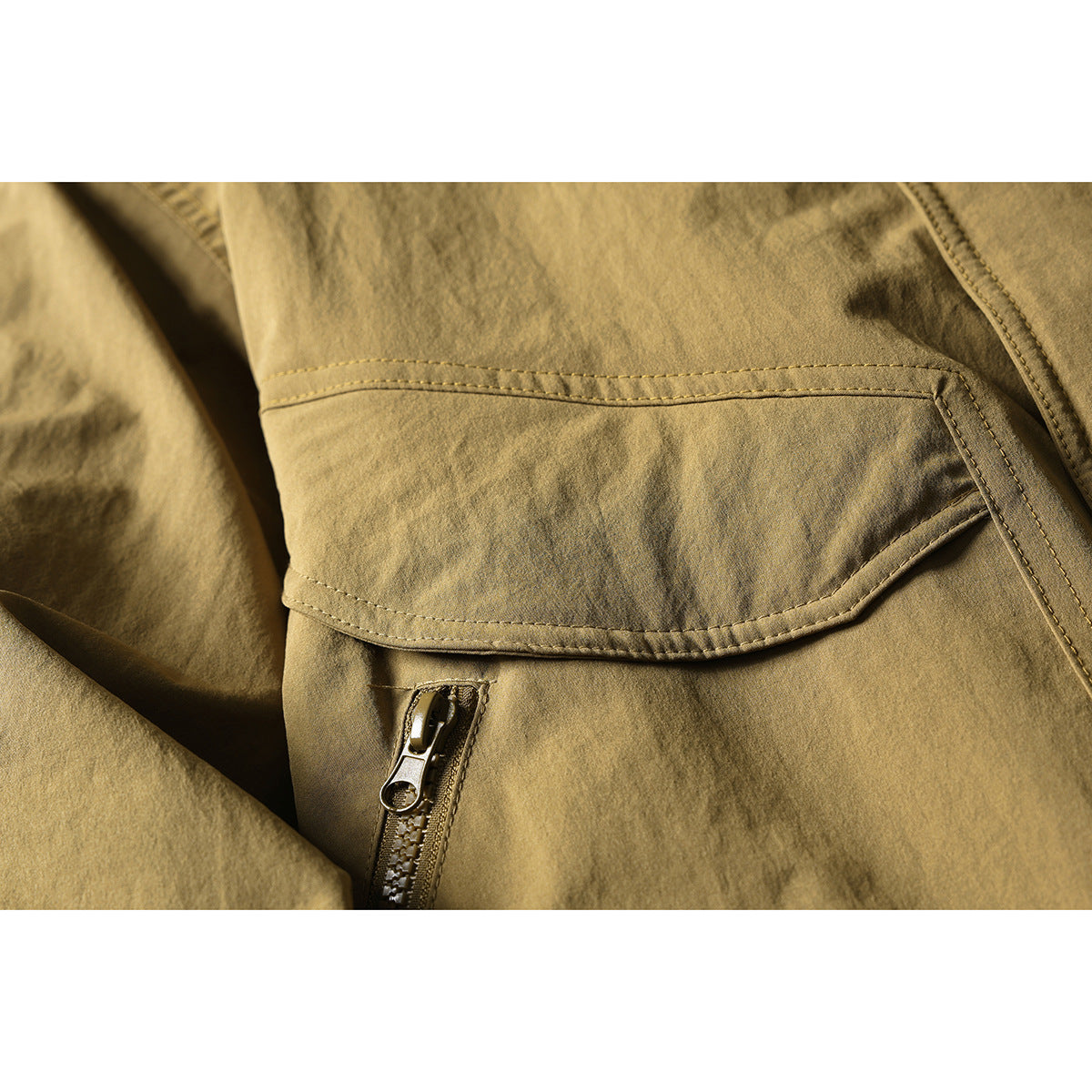 Close-up of a tan jacket's flap pocket, stitching, and zipper.