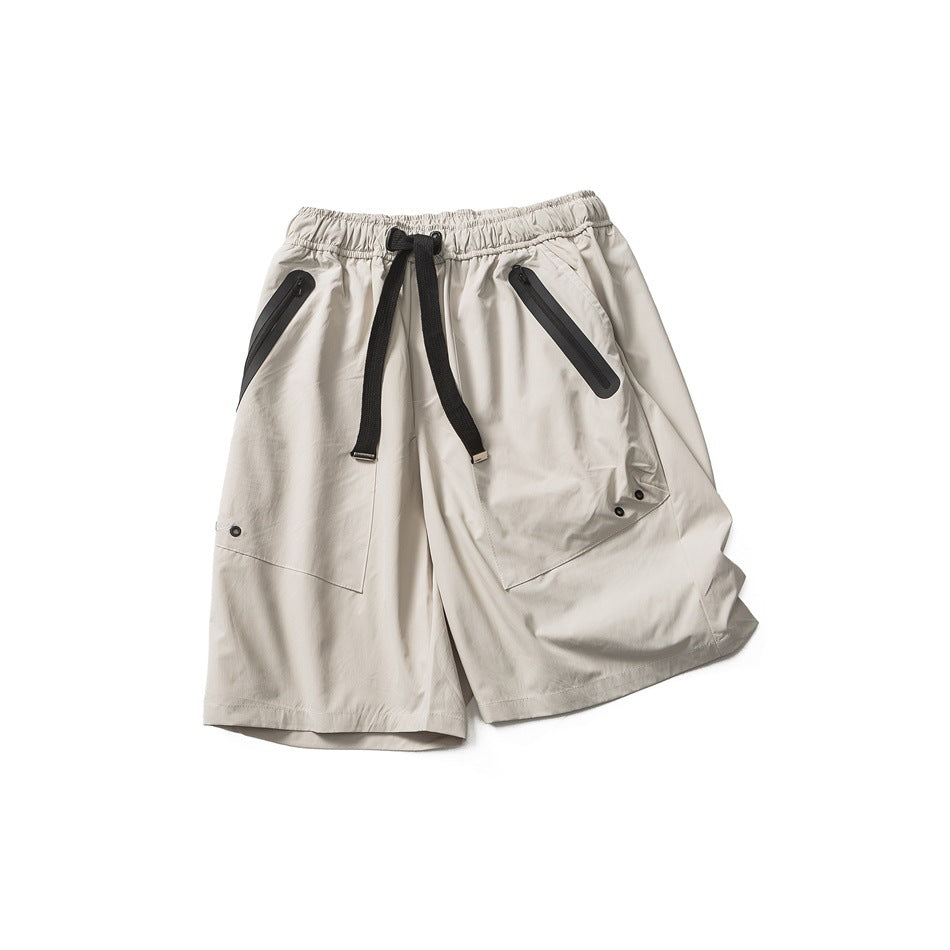 Beige-gray shorts laid at an angle showing zippered pockets, drawstring, front leg panel and metal eyelets