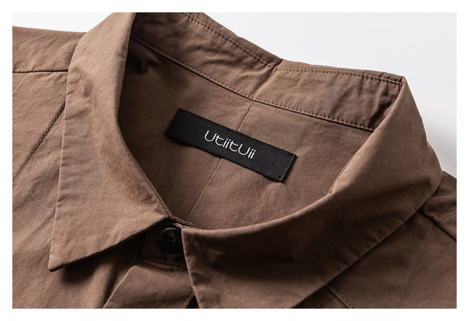 Close-up of a brown shirt collar, button, stitching, and black neck label.