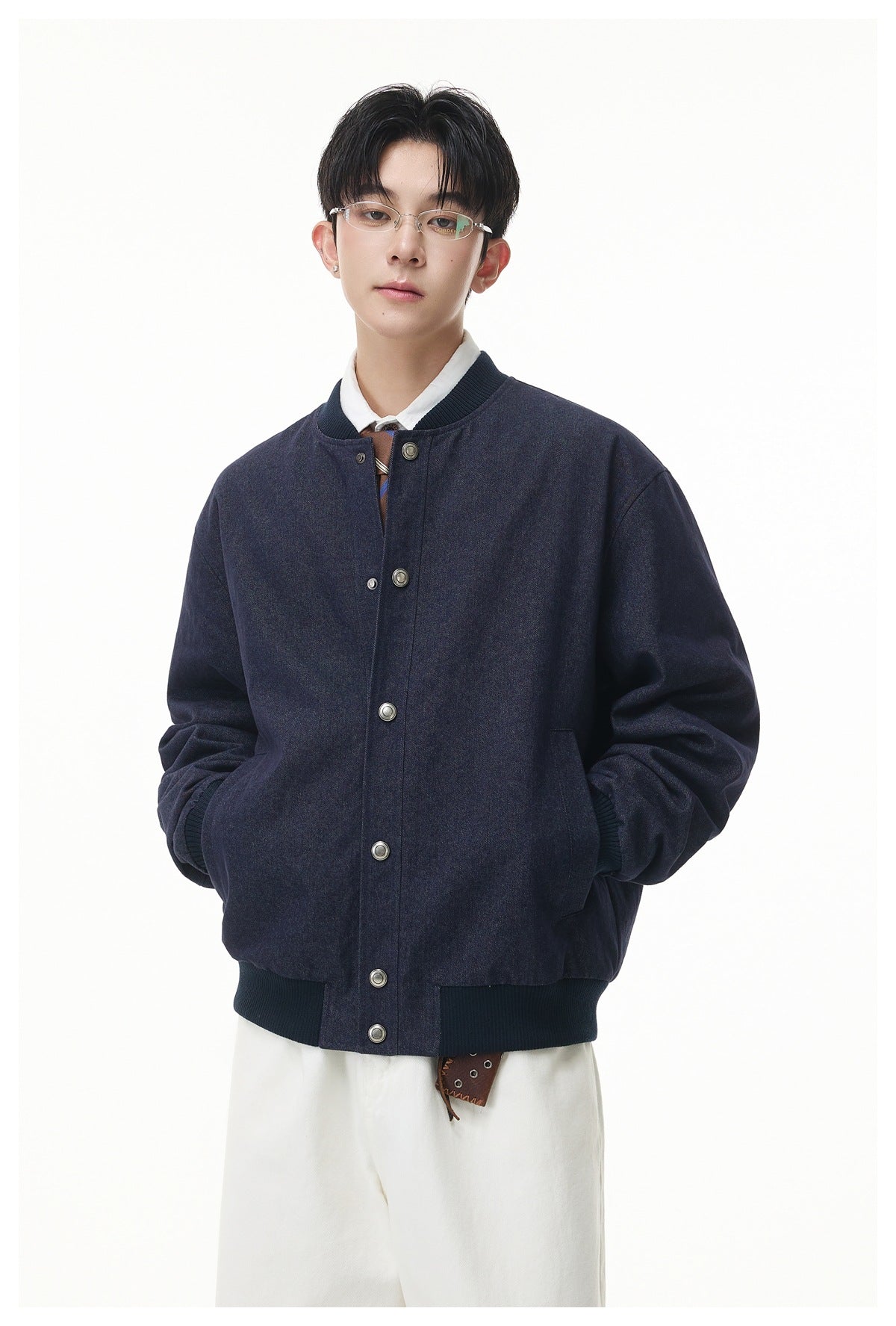 Model wearing a navy baseball-collar snap-front jacket over a white collared shirt with white pants, hands in pockets