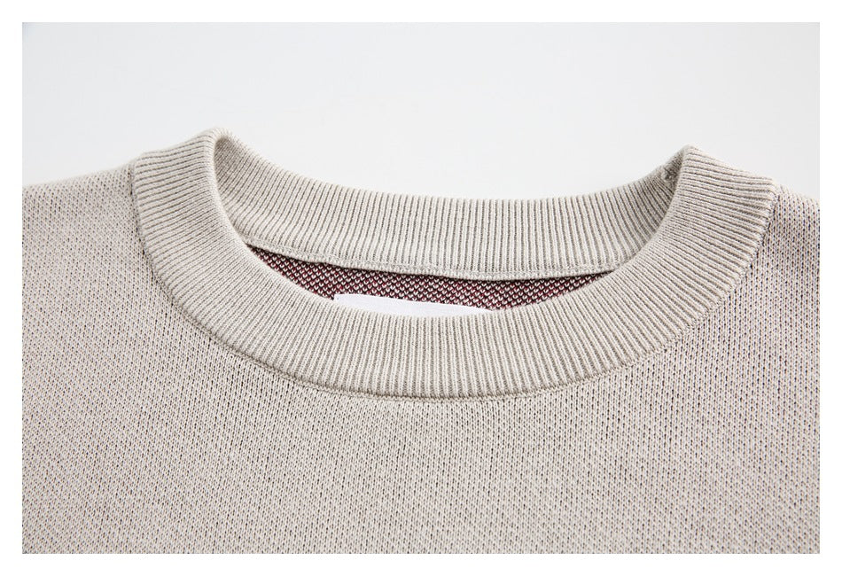 Close-up of a cream knit sweater's ribbed crew neckline and fine speckled texture.