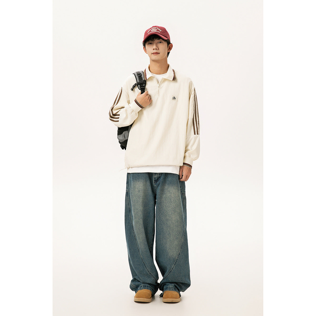 Front view of a model wearing a cream quarter-zip collared top with brown sleeve stripes and loose blue jeans.