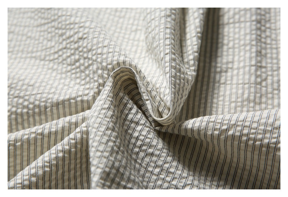Close-up of softly folded cream fabric with narrow dark pinstripes.