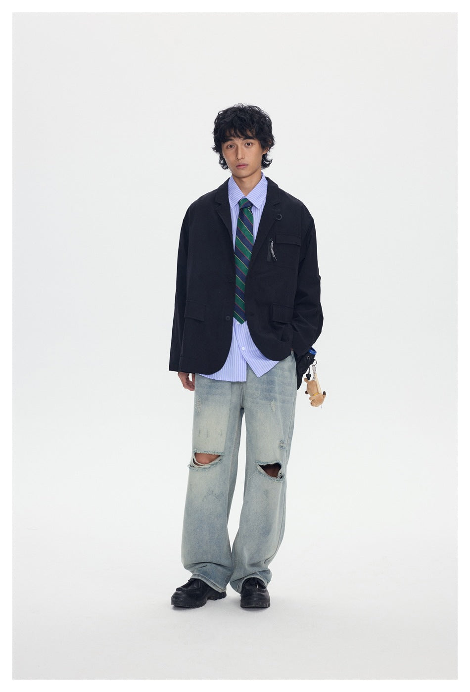 Model wearing a black blazer-style jacket over a striped shirt and tie with distressed light-wash jeans
