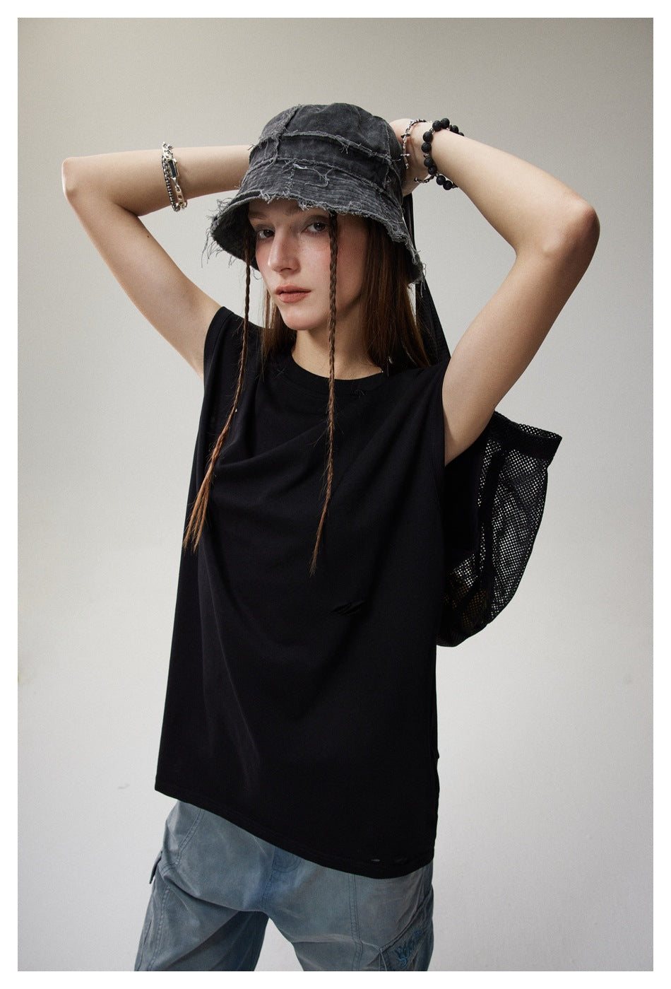 Model wearing a loose black sleeveless top with distressed slits, paired with pale blue jeans.