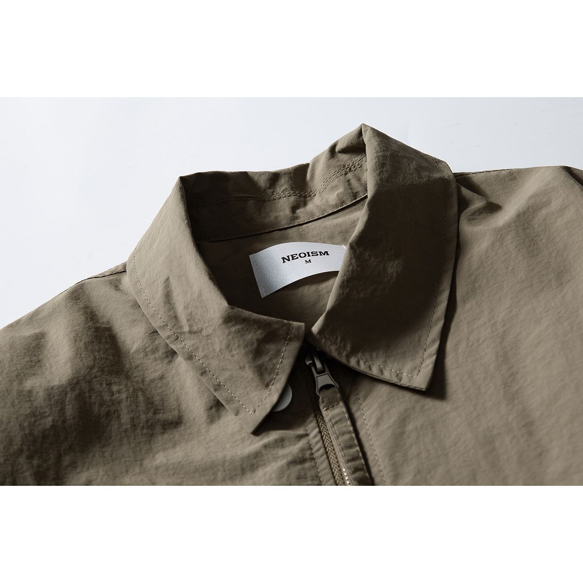 Close-up of an olive-gray jacket collar, zipper, and sewn-in neck label.