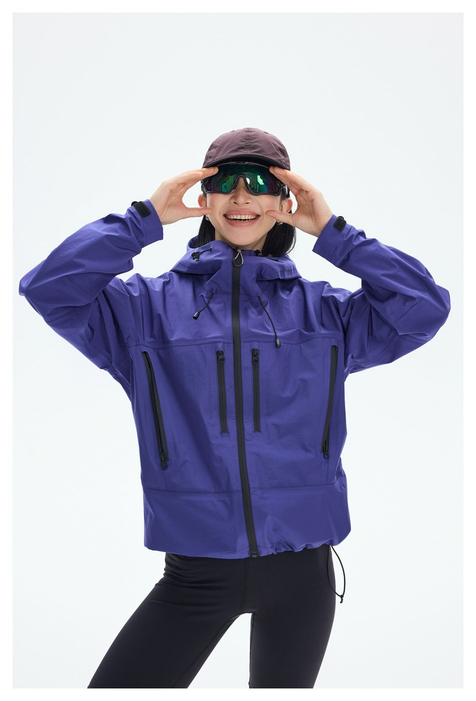 A woman models a purple hooded jacket with a front zipper and several black zip pockets.