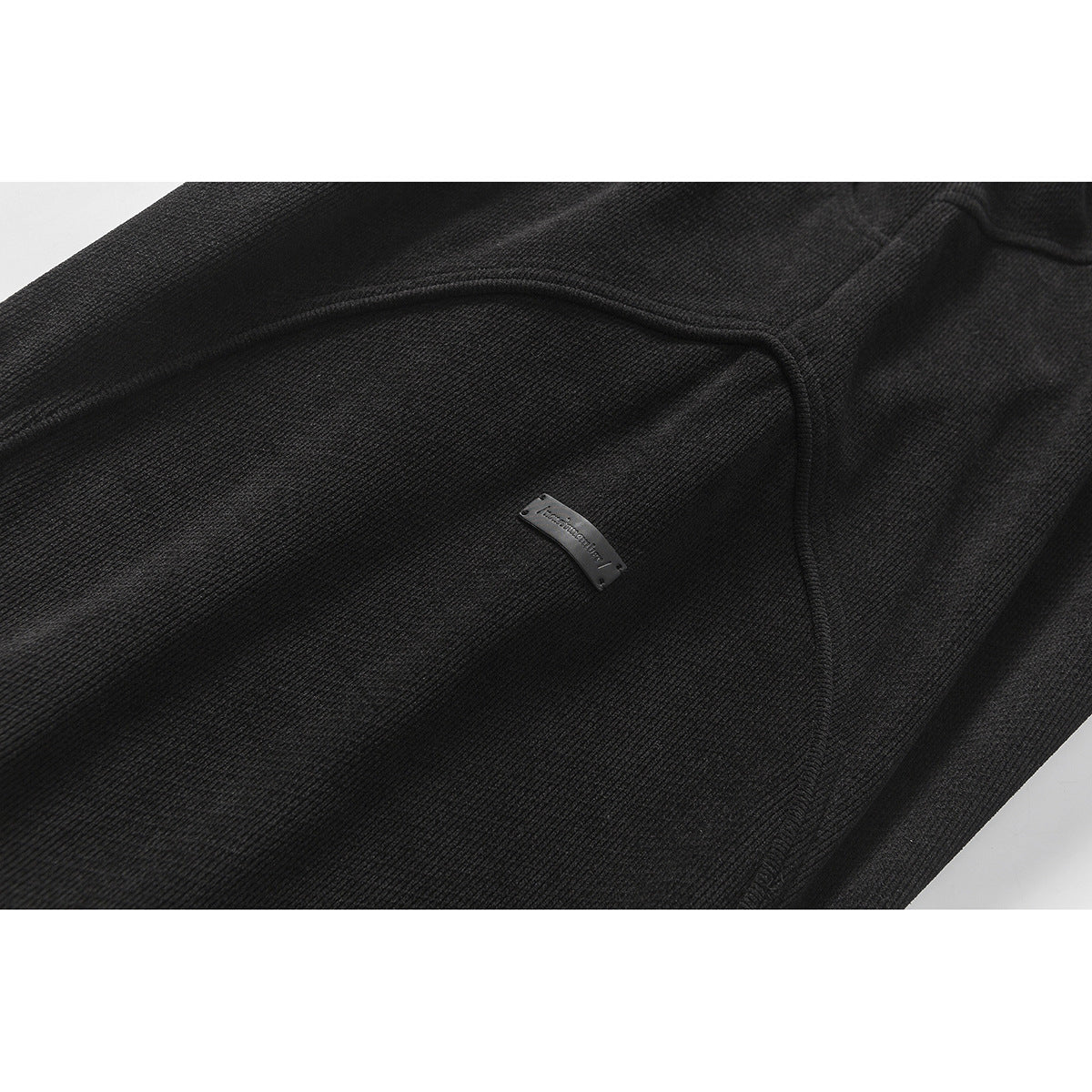 Close-up of black pants showing a curved seam and small metal garment label.