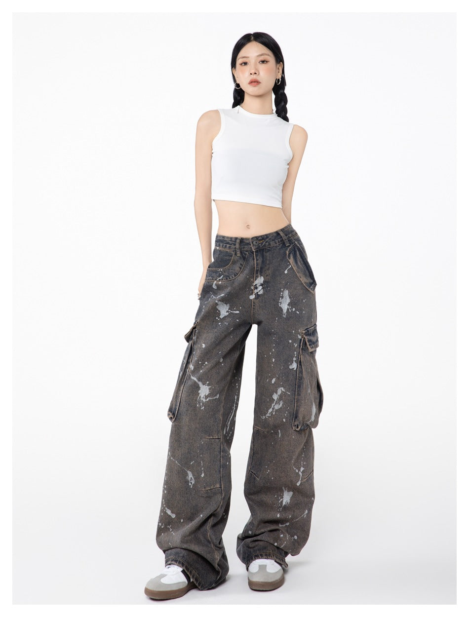 Model wearing wide-leg paint-splatter cargo jeans with a white sleeveless crop top and gray sneakers, front view