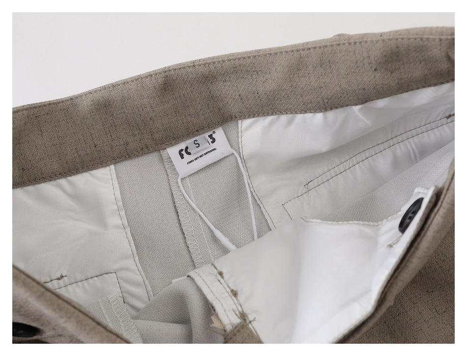 Close-up of beige-gray trousers opened at the waistband, showing the lining, seams, button, and sewn-in label.