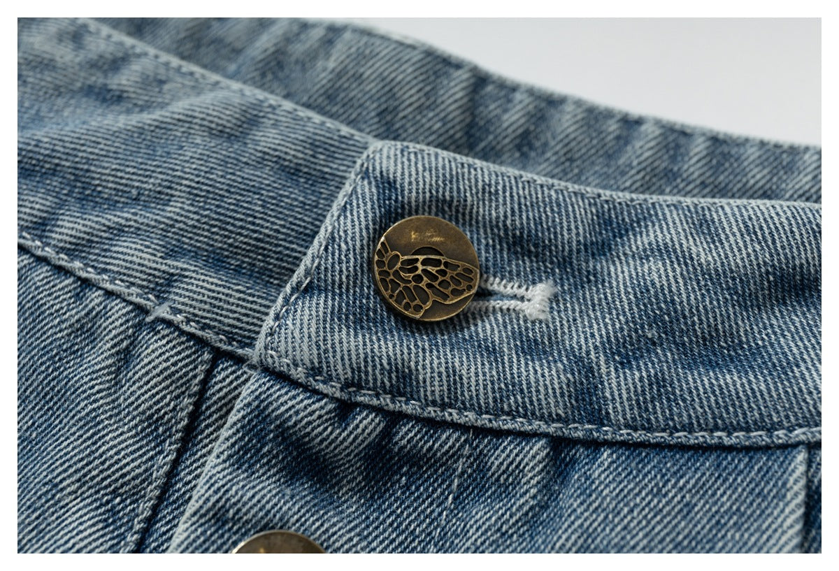 Close-up of blue denim waistband with a bronze-toned button featuring a cutout motif.