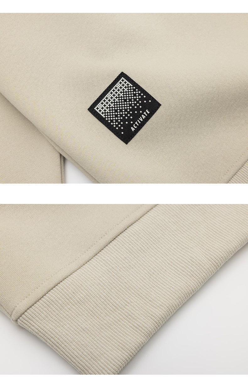 Close-up of a beige sweatshirt sleeve showing a black square “ACTIVATE” patch and a ribbed cuff.