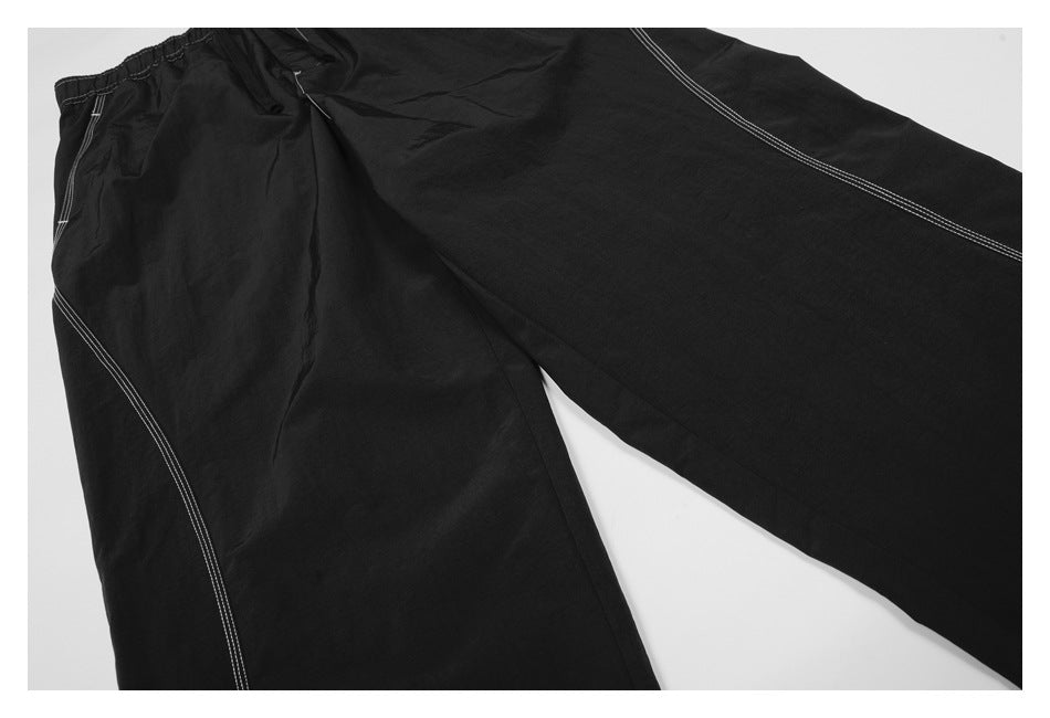 Close-up of black trousers laid flat, showing white contrast stitching along the seams.