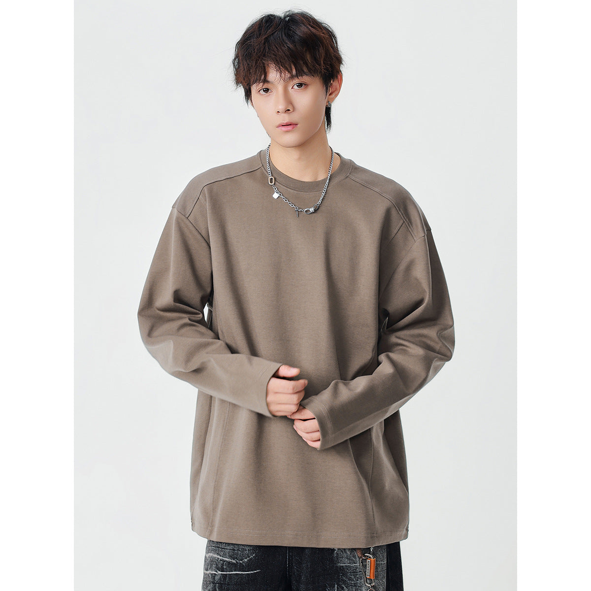 Model wearing an oversized taupe long-sleeve crewneck top with seamed shoulders.