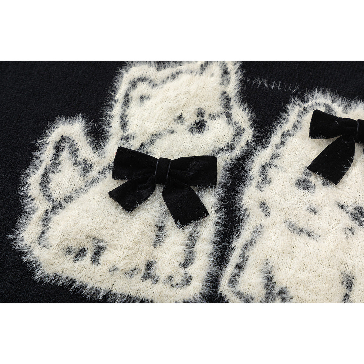 Close-up of two fuzzy white cat motifs with black bows on a black sweater.