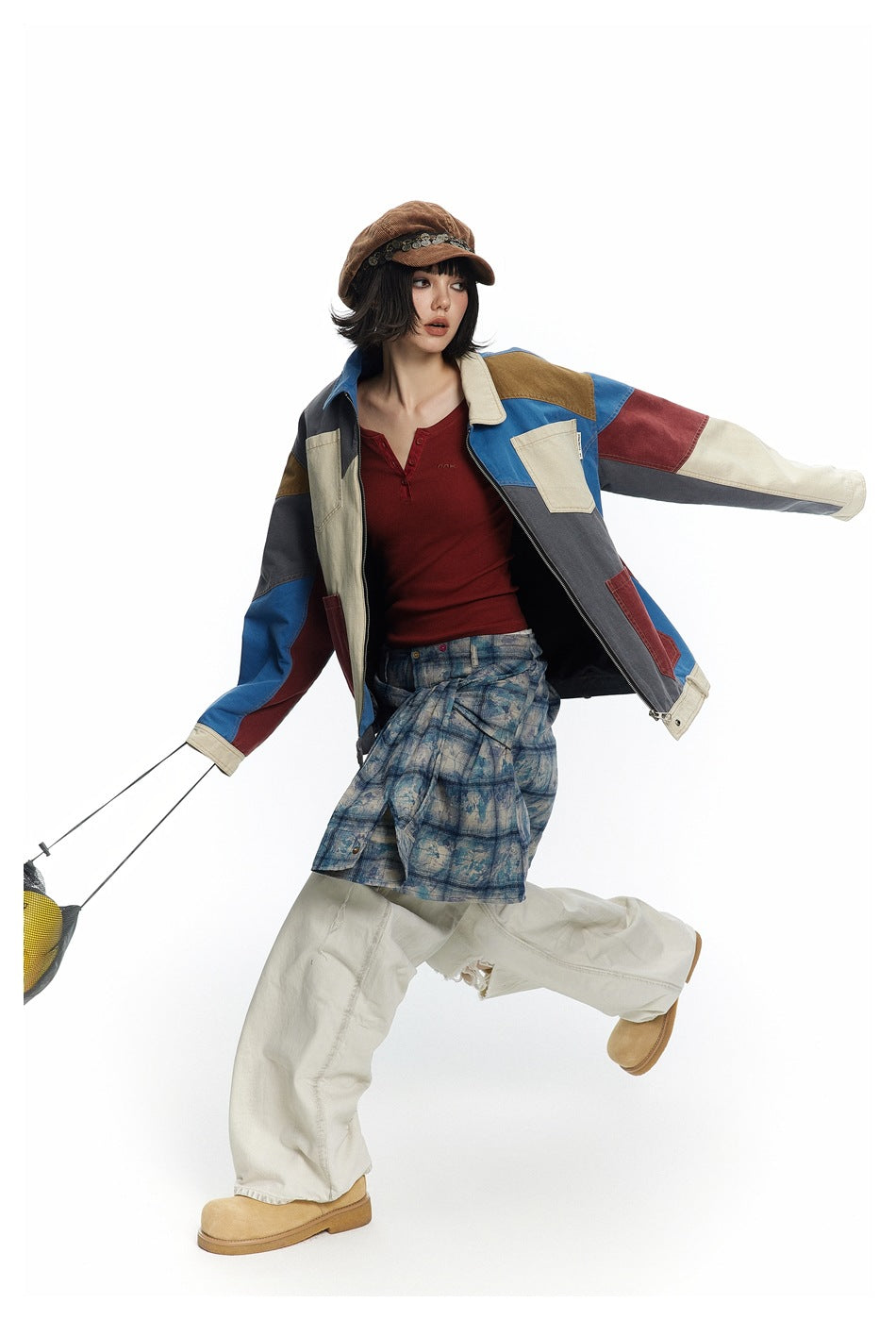 Model wearing an open multicolor patchwork jacket with a red top and blue plaid skirt, posed with arms extended.